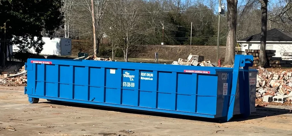 The Dumpster Co. 20 yard concrete roll-off dumpster on a demolition job site with brick and block debris