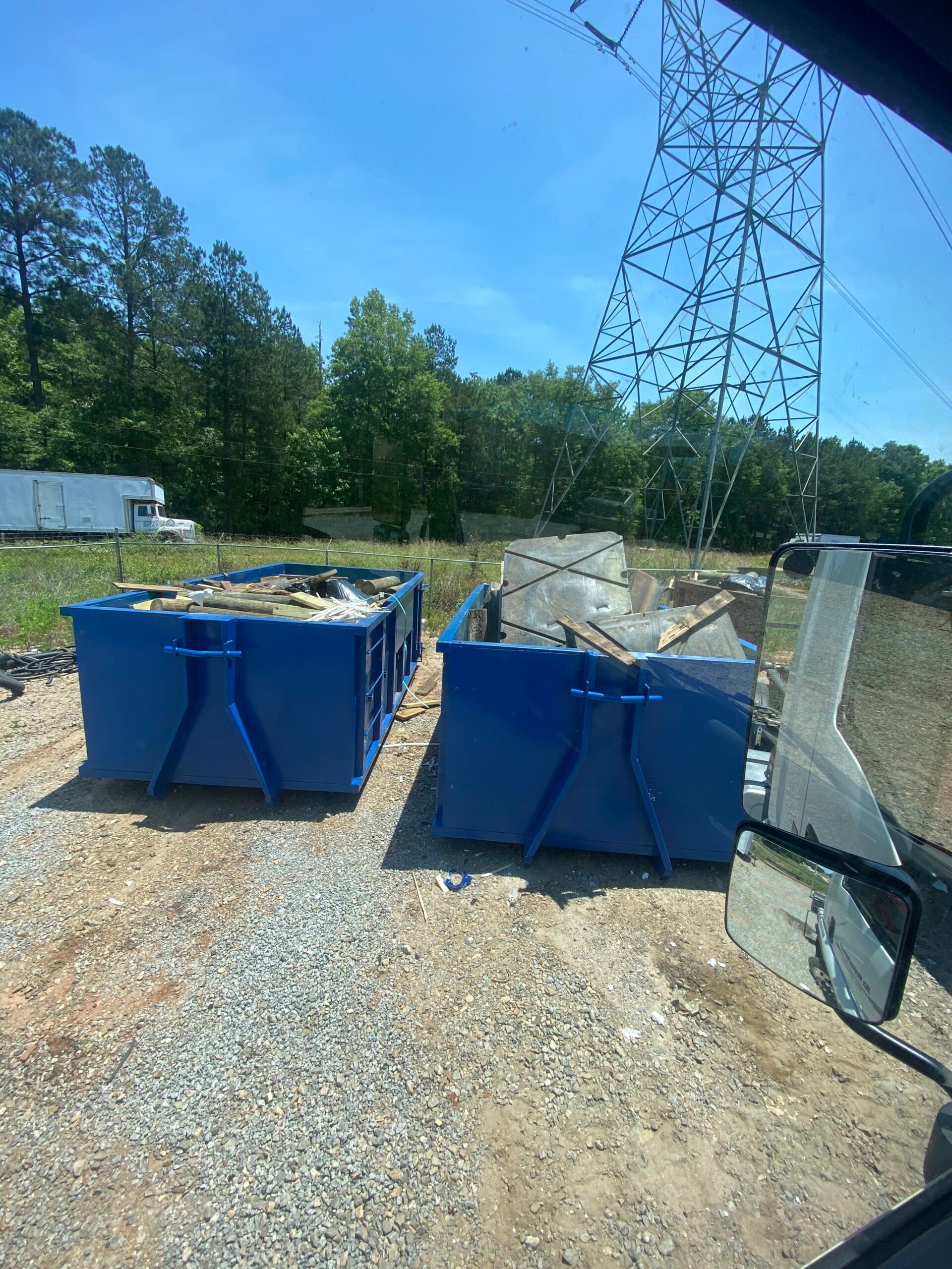 Two blue roll-off dumpsters filled with debris on a gravel job site