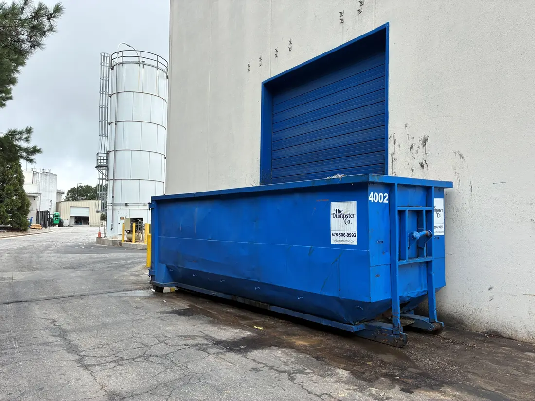 Blue roll-off dumpster beside a commercial building