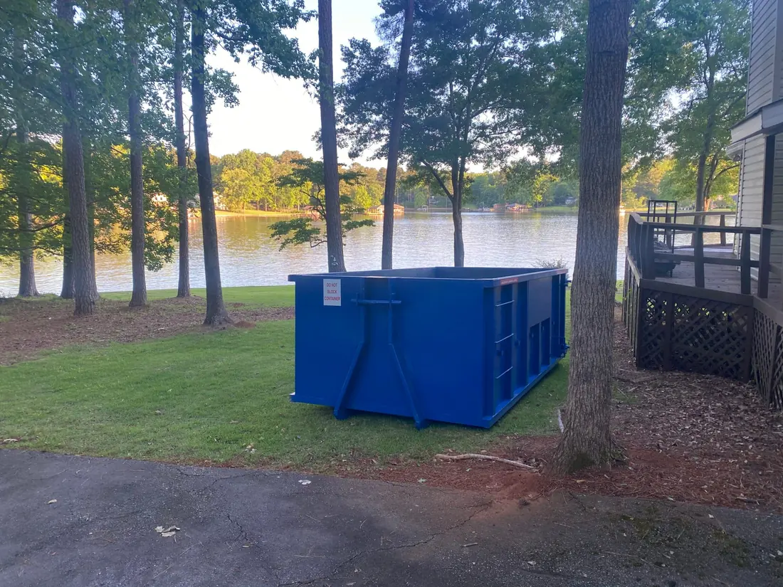 Blue roll-off dumpster on a lawn at a lakefront home