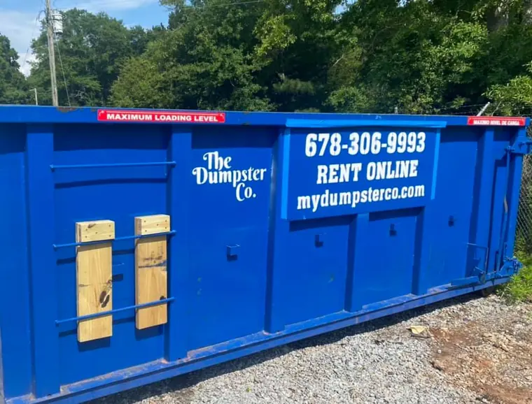 Blue The Dumpster Co. roll-off dumpster with phone number and website on the side