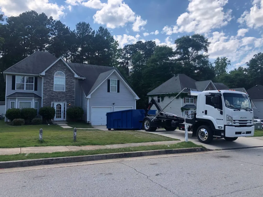 Roll-off truck delivering a blue dumpster to a home driveway