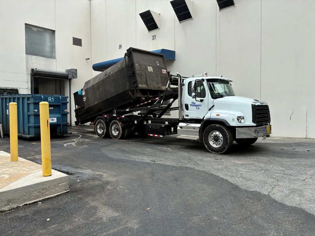 The Dumpster Co. truck hauling a loaded roll-off container from a commercial site
