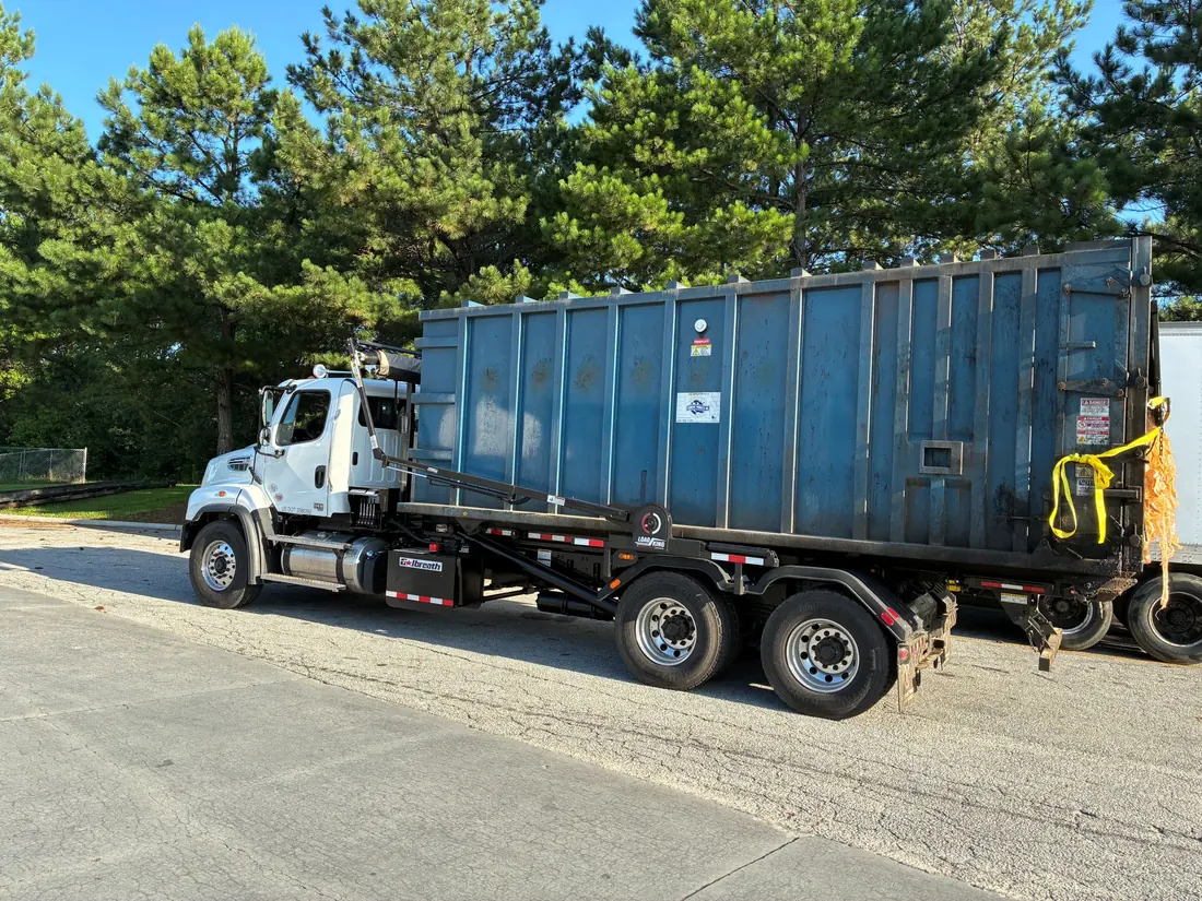 Roll-off truck hauling a large steel container on a paved lot