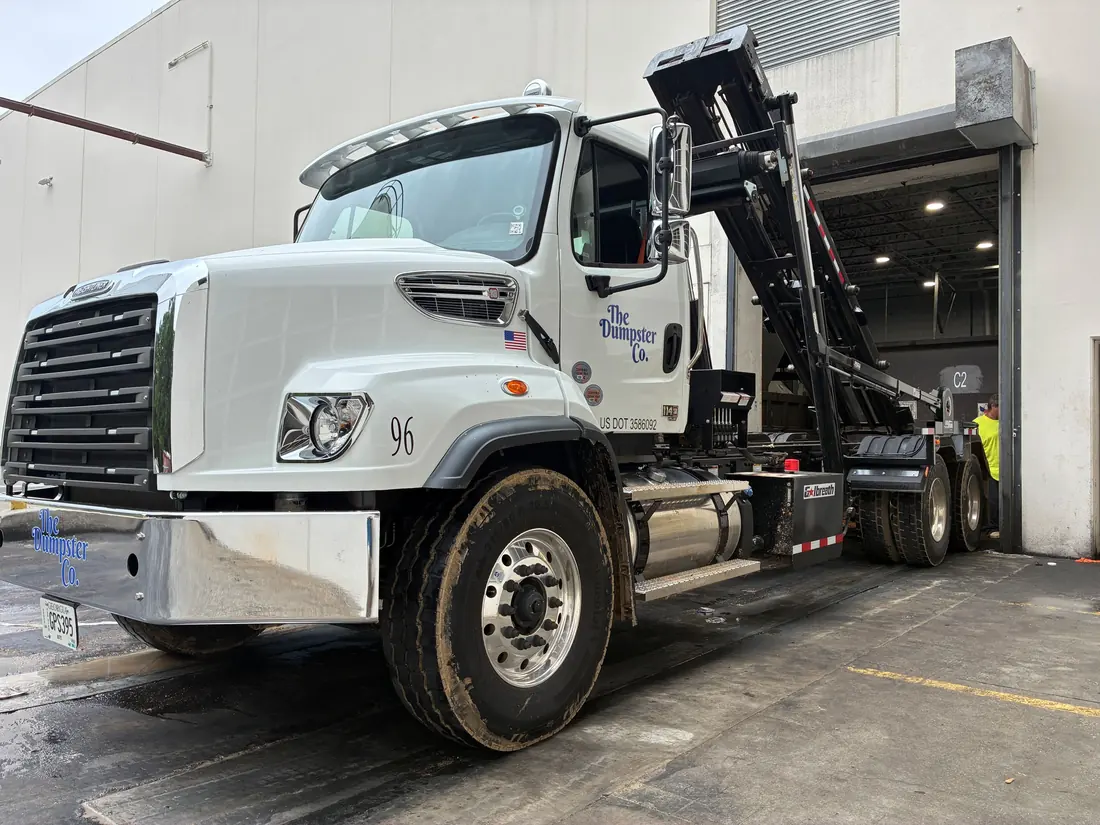 The Dumpster Co. roll-off truck lifting a container at a warehouse dock
