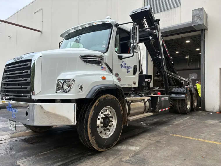 The Dumpster Co. roll-off truck lifting a container at a warehouse dock