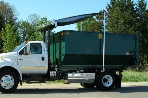Roll-off truck carrying a tarped green dumpster