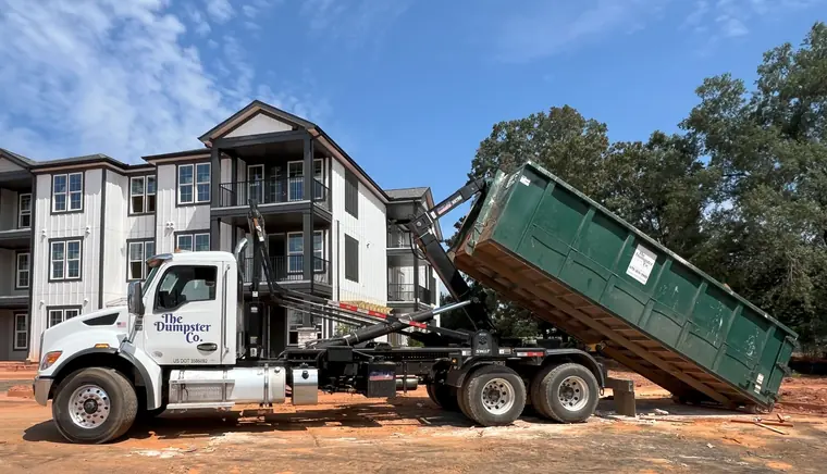 The Dumpster Co. truck unloading a green roll-off dumpster at an apartment construction site